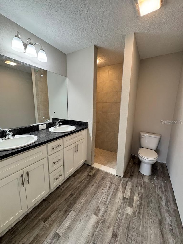 bathroom featuring wood finished floors, walk in shower, toilet, double vanity, and a textured ceiling
