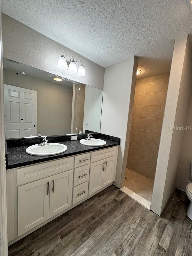 bathroom featuring wood finished floors, a walk in shower, double vanity, toilet, and a textured ceiling