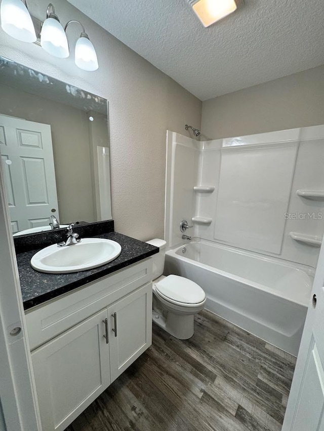 full bathroom featuring a textured ceiling, wood finished floors, shower / washtub combination, vanity, and toilet
