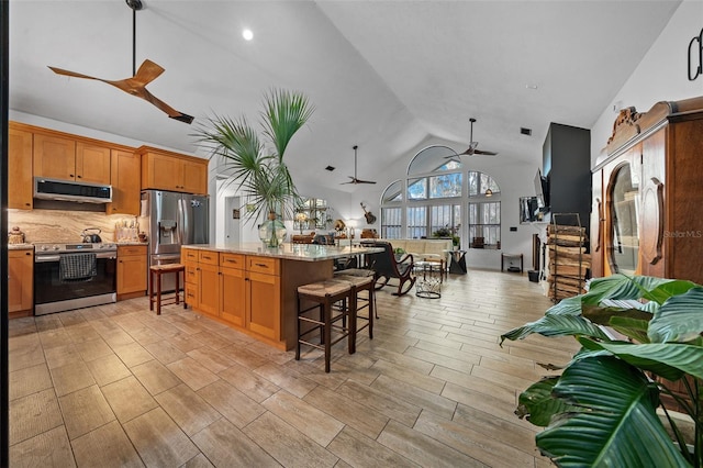 kitchen with a kitchen island, appliances with stainless steel finishes, a breakfast bar, range hood, and ceiling fan