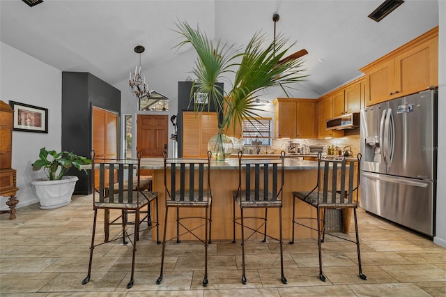 kitchen with stainless steel appliances, a kitchen breakfast bar, a center island, decorative light fixtures, and vaulted ceiling