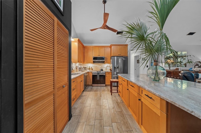 kitchen with sink, ceiling fan, stainless steel appliances, light stone countertops, and backsplash