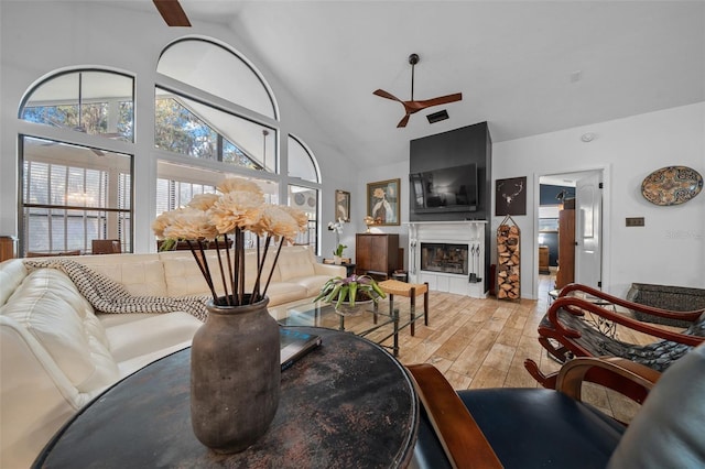 living room featuring hardwood / wood-style floors, high vaulted ceiling, a tile fireplace, and ceiling fan