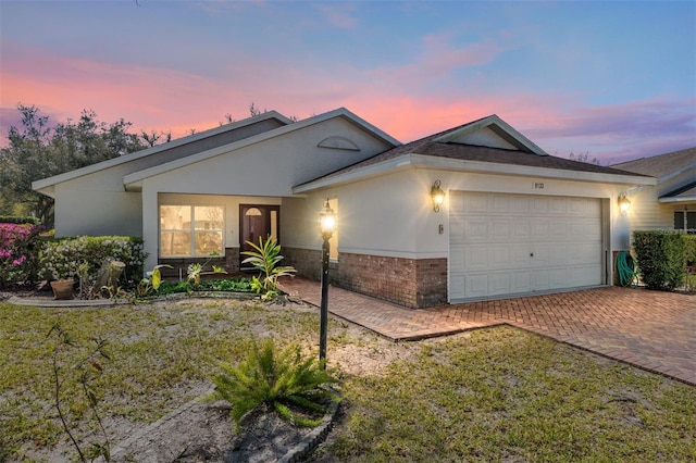 single story home with brick siding, stucco siding, an attached garage, and decorative driveway