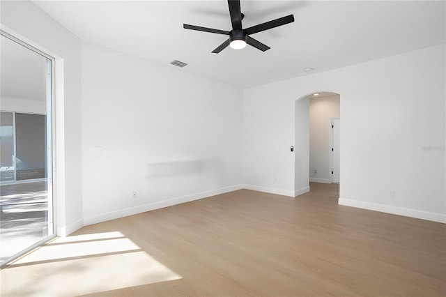 unfurnished room featuring arched walkways, visible vents, light wood-style flooring, and baseboards