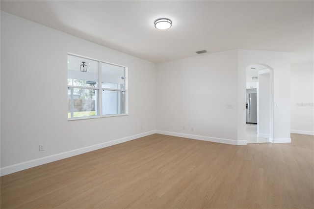 spare room featuring baseboards, light wood-style floors, visible vents, and arched walkways