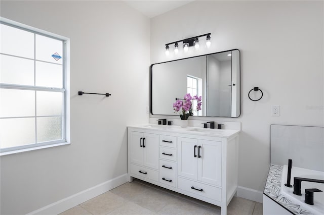 full bath with double vanity, a healthy amount of sunlight, and baseboards