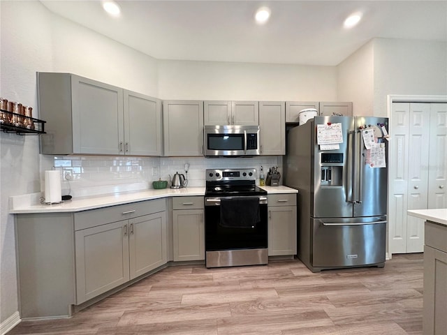 kitchen featuring backsplash, gray cabinets, light hardwood / wood-style floors, and appliances with stainless steel finishes