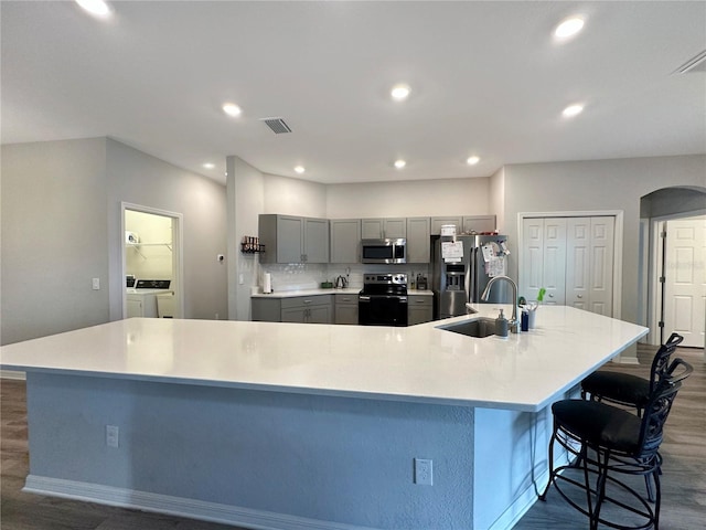 kitchen featuring a breakfast bar, washer and dryer, a large island with sink, appliances with stainless steel finishes, and gray cabinets