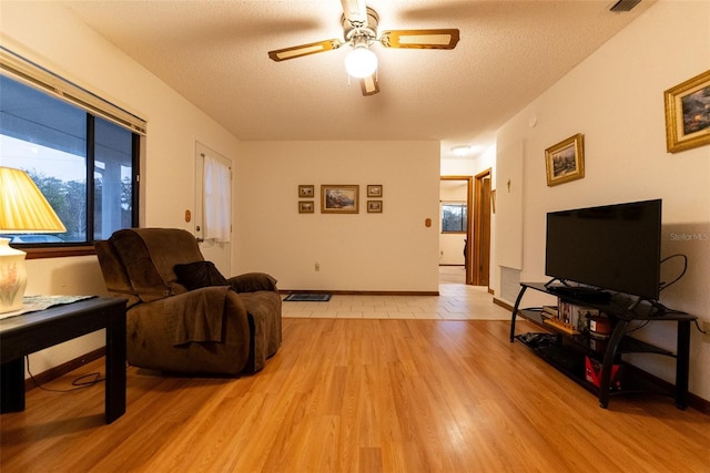 living room with ceiling fan, a textured ceiling, and light hardwood / wood-style flooring