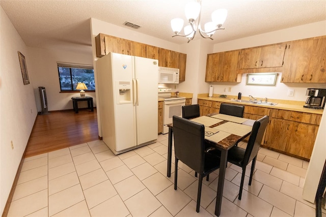 kitchen featuring sink, an inviting chandelier, a textured ceiling, pendant lighting, and white appliances