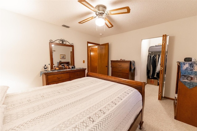 bedroom featuring ceiling fan, a textured ceiling, a walk in closet, light colored carpet, and a closet
