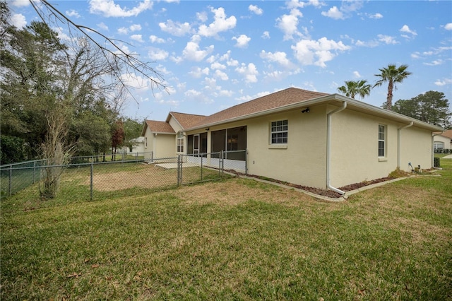 rear view of house featuring stucco siding, a lawn, fence private yard, and a sunroom