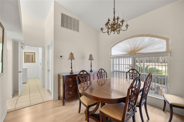 dining room with baseboards, visible vents, light wood finished floors, high vaulted ceiling, and a notable chandelier