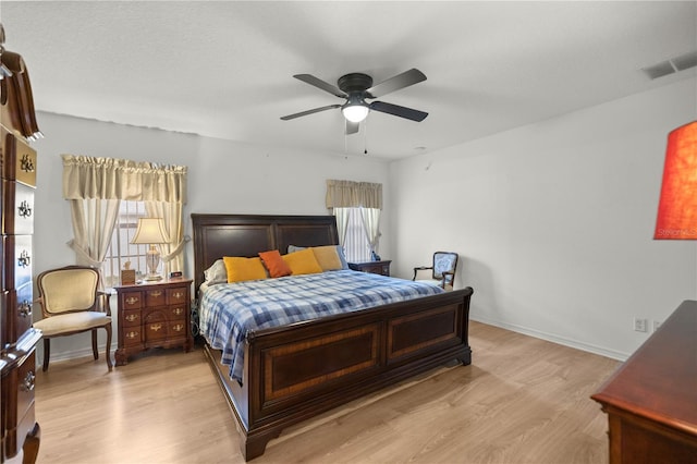 bedroom featuring a ceiling fan, light wood-style floors, visible vents, and baseboards