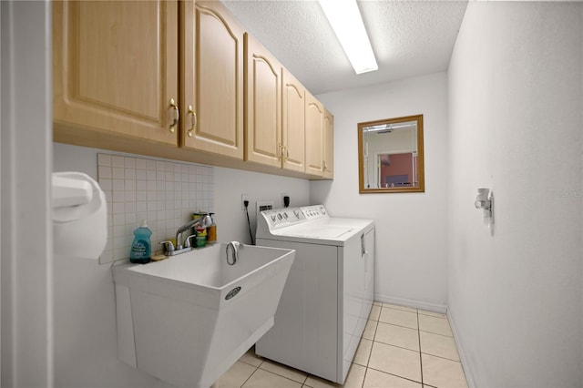 clothes washing area featuring a sink, a textured ceiling, cabinet space, separate washer and dryer, and light tile patterned flooring