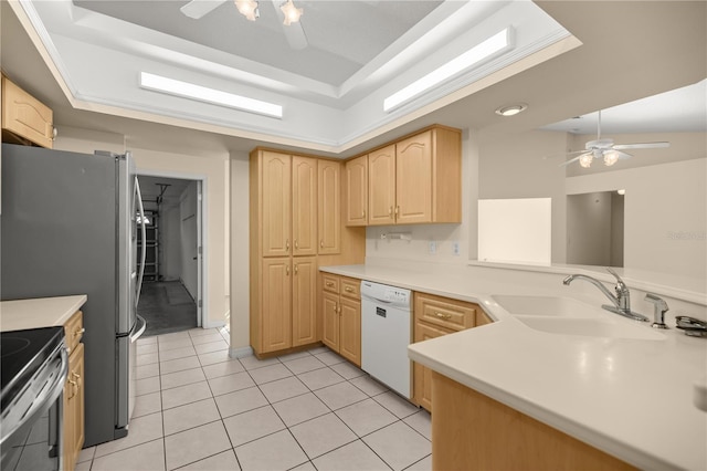 kitchen with a sink, ceiling fan, a tray ceiling, light brown cabinetry, and dishwasher