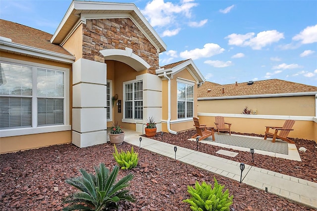 property entrance featuring a patio area, stone siding, and stucco siding