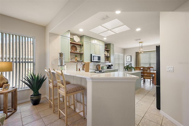 kitchen featuring green cabinetry, a peninsula, open shelves, light countertops, and stainless steel microwave