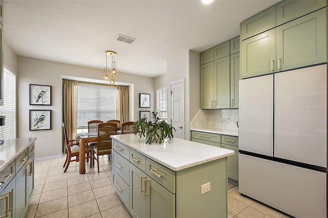 kitchen with refrigerator, green cabinetry, a kitchen island, decorative light fixtures, and light tile patterned flooring