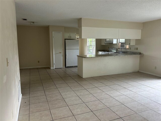 kitchen with white appliances, kitchen peninsula, a textured ceiling, and white cabinets