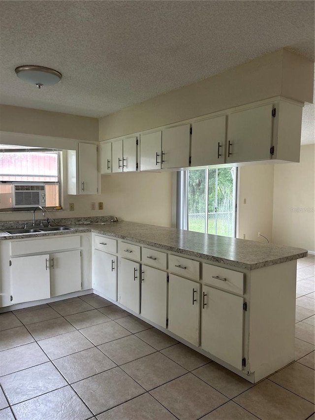 kitchen featuring sink, white cabinets, light tile patterned floors, kitchen peninsula, and a textured ceiling