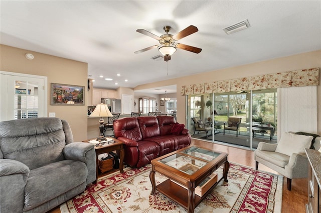 living room featuring ceiling fan with notable chandelier, light wood finished floors, visible vents, and recessed lighting