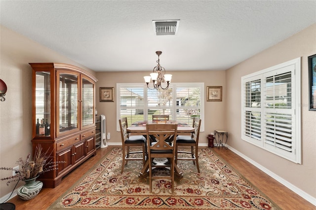 dining room with a notable chandelier, a textured ceiling, visible vents, and wood finished floors