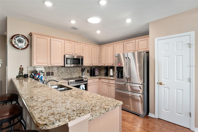 kitchen with stainless steel appliances, decorative backsplash, light brown cabinets, a sink, and a peninsula