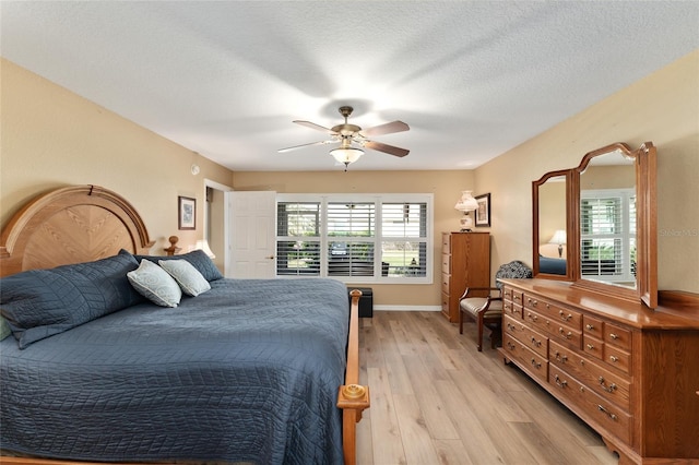 bedroom with a textured ceiling, ceiling fan, multiple windows, and light wood-style floors