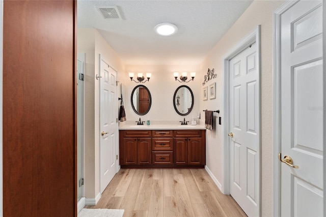 full bathroom with double vanity, visible vents, a sink, and wood finished floors