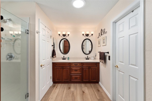 bathroom featuring a sink, wood finished floors, baseboards, double vanity, and a stall shower