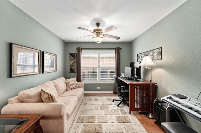 office area with a textured wall, ceiling fan, light wood-style flooring, and baseboards