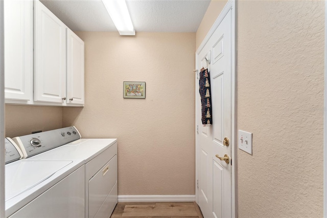 laundry room featuring light wood finished floors, cabinet space, a textured wall, separate washer and dryer, and baseboards