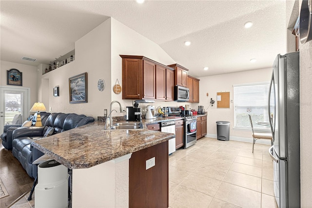 kitchen with sink, appliances with stainless steel finishes, dark stone countertops, a kitchen bar, and kitchen peninsula