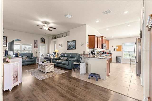 living room with lofted ceiling, a textured ceiling, ceiling fan, and light hardwood / wood-style flooring