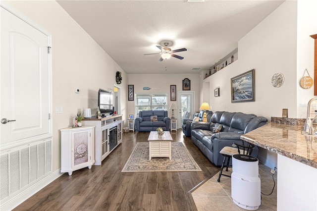 living room with ceiling fan, dark hardwood / wood-style floors, and a textured ceiling