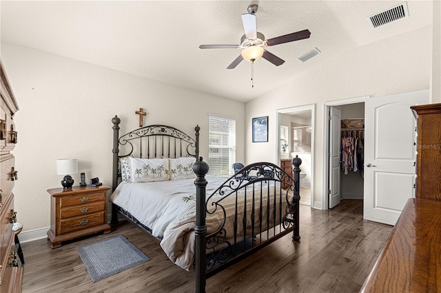 bedroom with connected bathroom, a walk in closet, vaulted ceiling, dark hardwood / wood-style floors, and ceiling fan