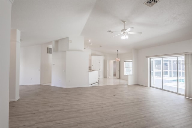 unfurnished living room with ceiling fan with notable chandelier, light hardwood / wood-style flooring, high vaulted ceiling, and a textured ceiling