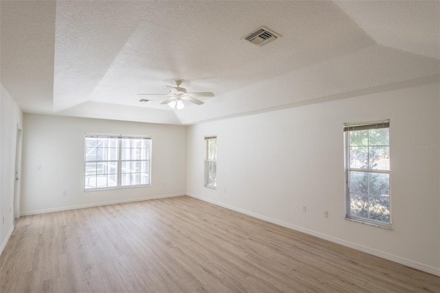 unfurnished room with plenty of natural light, a raised ceiling, light hardwood / wood-style flooring, and a textured ceiling