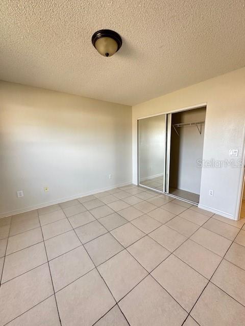 unfurnished bedroom featuring a textured ceiling, a closet, and light tile patterned floors