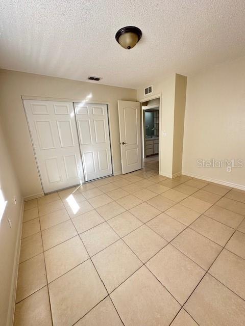 unfurnished bedroom with a textured ceiling, a closet, and light tile patterned floors