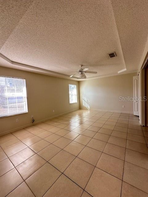 tiled spare room featuring a tray ceiling, a textured ceiling, and ceiling fan