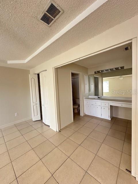 unfurnished bedroom with built in desk, a textured ceiling, a closet, and light tile patterned floors