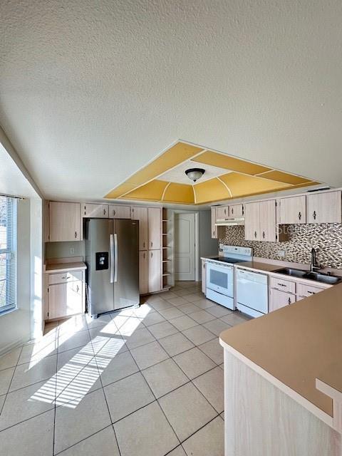 kitchen featuring a textured ceiling, light tile patterned floors, backsplash, and white appliances