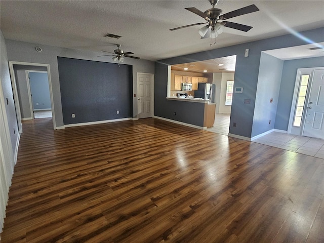 unfurnished living room featuring ceiling fan, visible vents, dark wood finished floors, and baseboards
