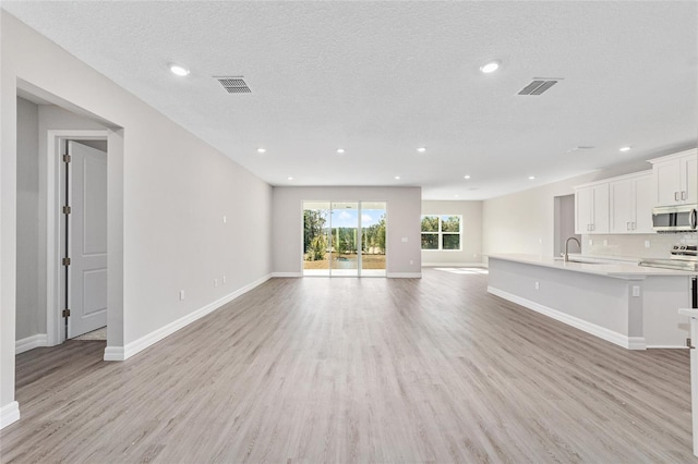 unfurnished living room featuring light hardwood / wood-style flooring, sink, and a textured ceiling