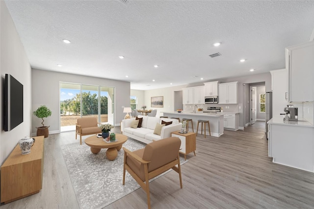 living room featuring light hardwood / wood-style floors, plenty of natural light, sink, and a textured ceiling