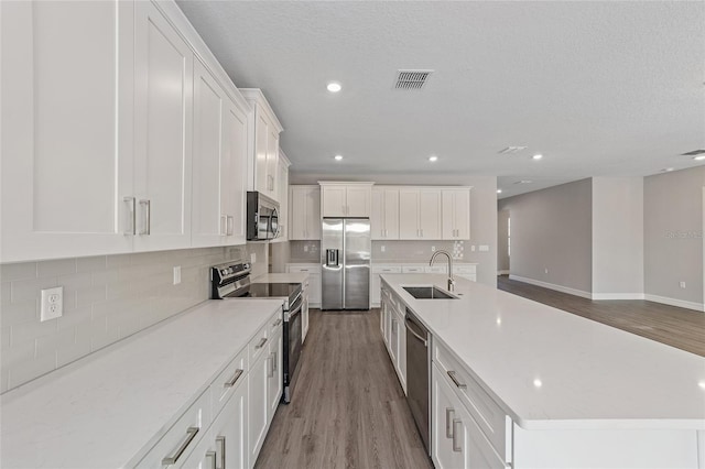 kitchen with appliances with stainless steel finishes, sink, light hardwood / wood-style flooring, a large island, and white cabinets