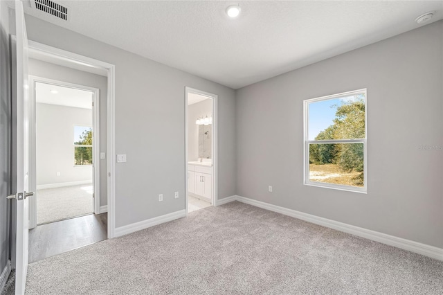 unfurnished bedroom featuring ensuite bath, carpet, and a textured ceiling